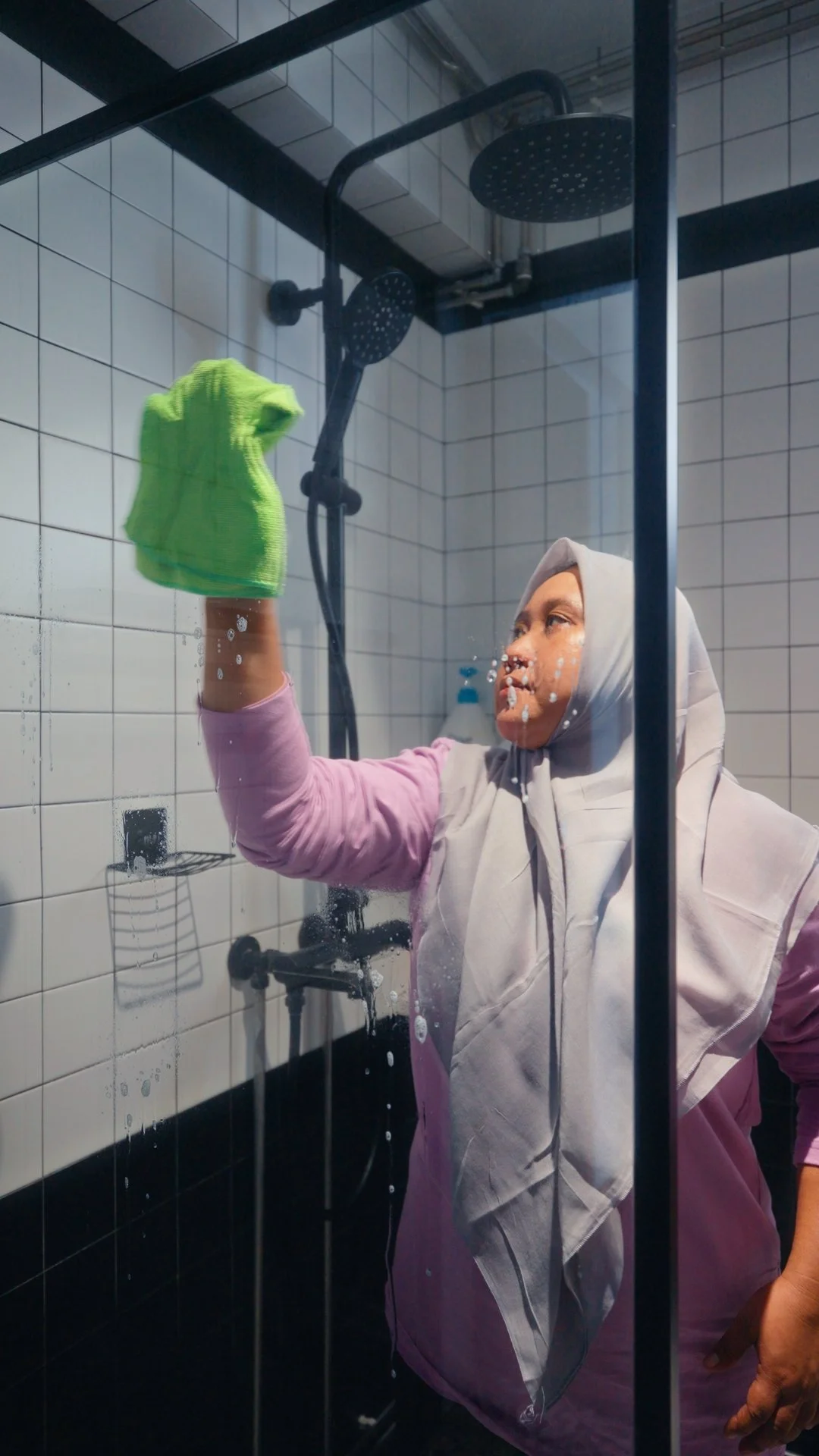 A Jaz Helpers helper cleaning a bathroom shower screen